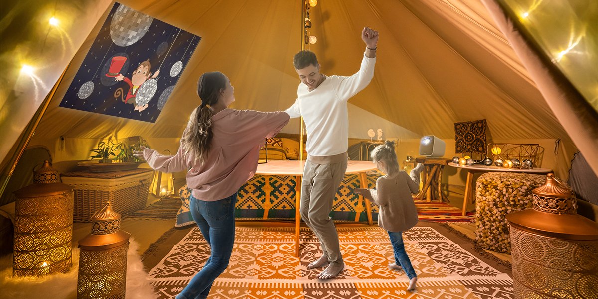 A family dancing to a projection on a tent with a portable projector when glamping 