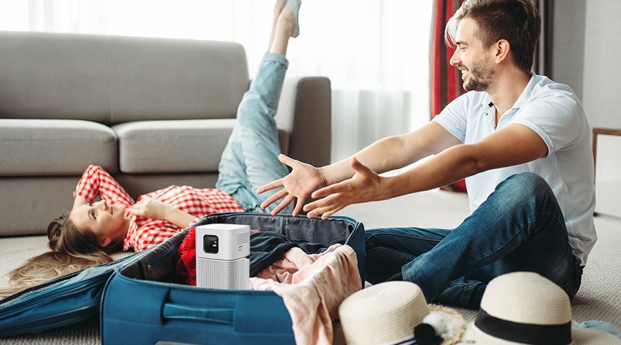 Young couple packing luggage for travel and include a portable projector for a leisure trip