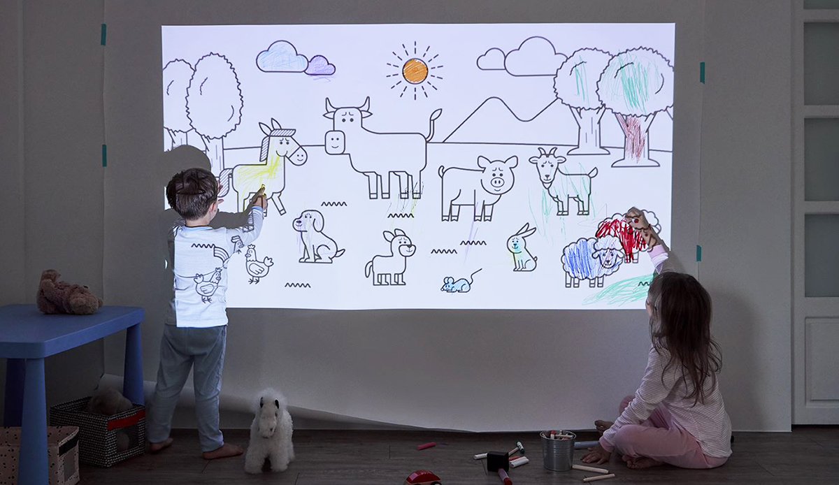 Two kids drawing on a big wall with the help of a portable projector