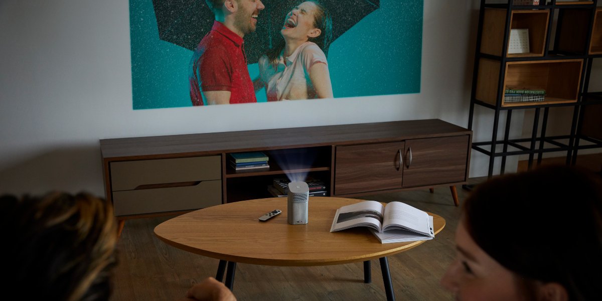 A portable projector displaying tv series on a white wall in a living room