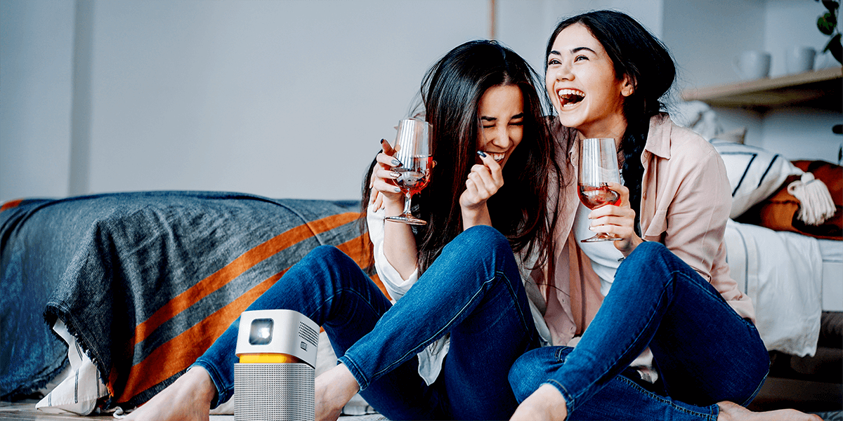 two girls enjoying big screen entertainment on a mini portable projector in a small room